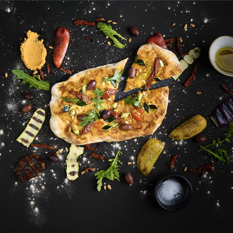 Belegte Pinsa mit bedda Frischcreme mediterrane Tomate, getrockneten Tomaten, Oliven, Grillgemüse, Rucola und geriebenem Käse