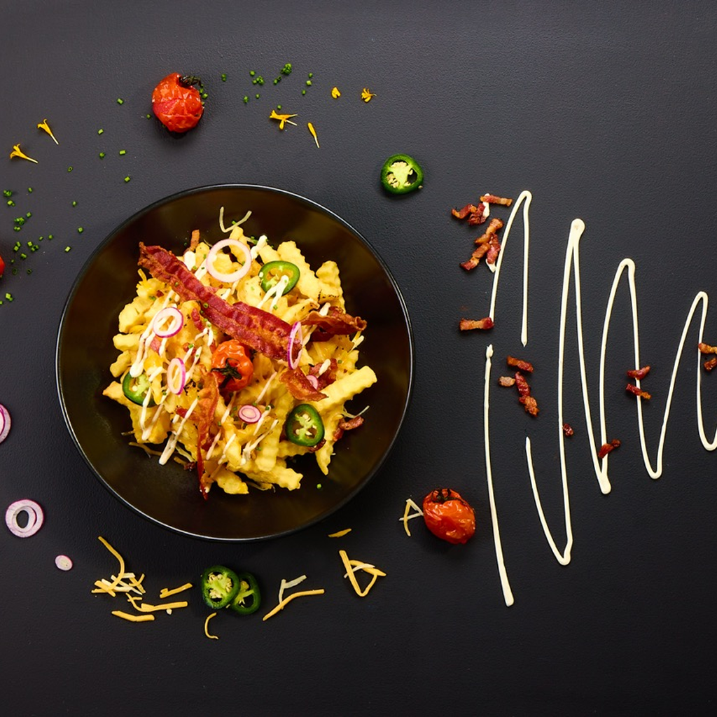 Knusprige Pommes frites übergossen mit Melted Cheese Dip, bestreut mit Bacon-Würfeln und grünen Jalapeños, mit Arizona Ranch Sauce in Linien aufgezogen und mit Schnittlauch-Ringen garniert