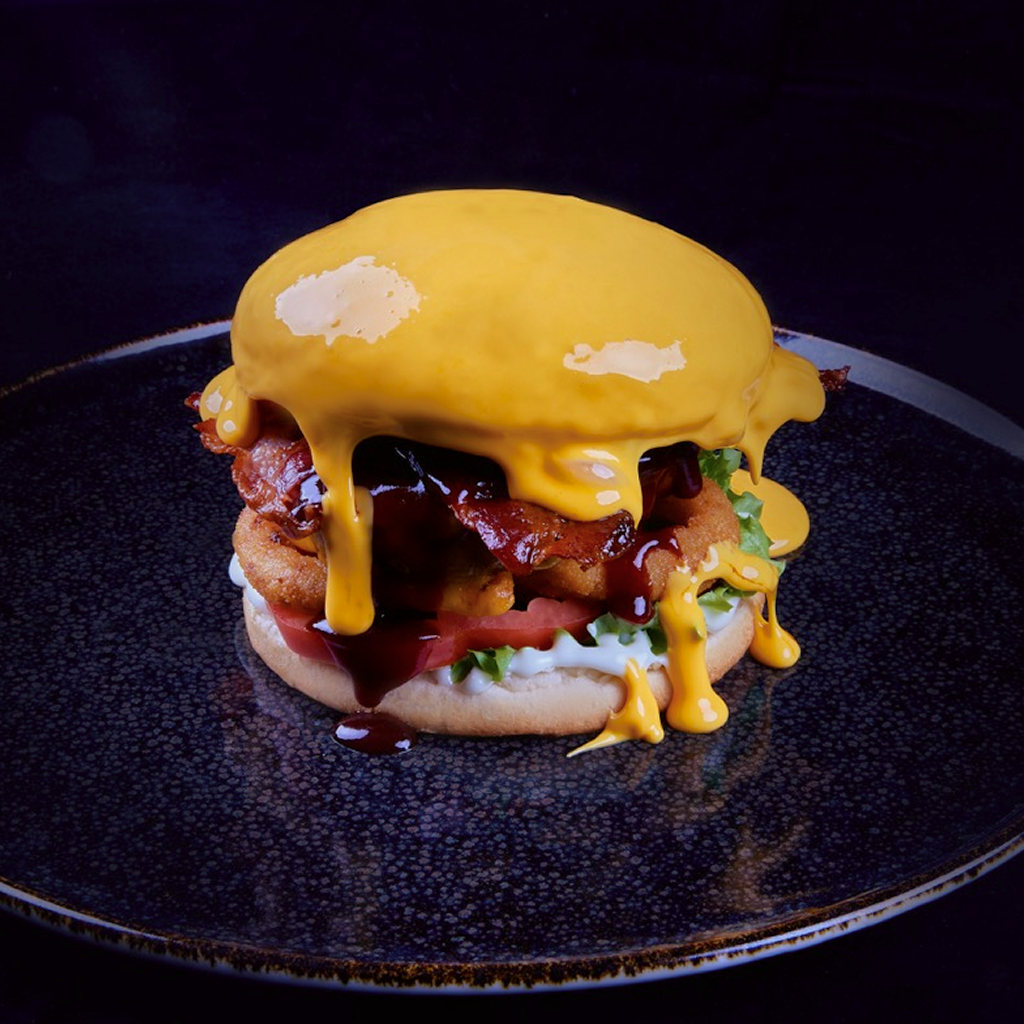 Burger mit Dry Aged Beef Patty, Cheddar, knusprigem Bacon, Zwiebelringen, Röstzwiebeln, Tomate, Lollo bionda, Trüffelmayo, BBQ Dip mit Biergeschmack und Chili Cheese Dip