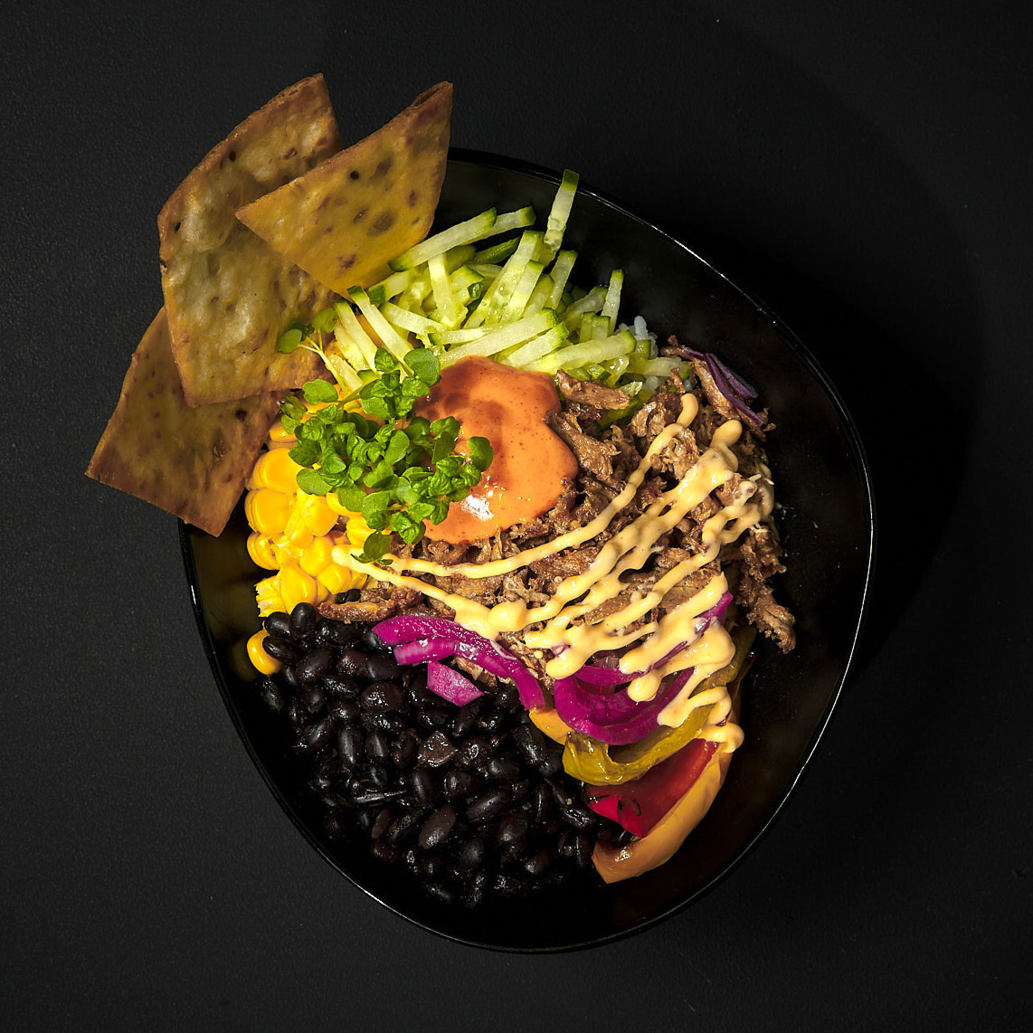 Tex-Mex-Bowl mit Langkornreis, Redefine PRO Pulled Pork, schwarzen Bohnen, Mais, Gurke, Paprika, Pink Onions, Smokey Chili Dip, White Smoked BBQ Dip, Kresse und Nacho Chips