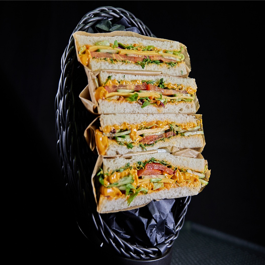 Belegtes Sandwich mit Mojo Rojo Dip, Rucola, bedda Cheddar Style, Tomaten, Gurke und Mixsalat