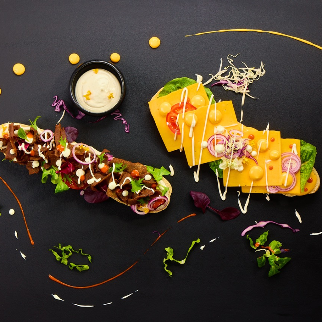 Aufgeschnittenes Baguette belegt mit Kalbs-Dönerfleisch, geschmolzenem Cheddar, Radicchio, Romana-Salat, Tomaten, roten Zwiebeln, Rotkohl und einem Streifen Arizona Ranch Sauce