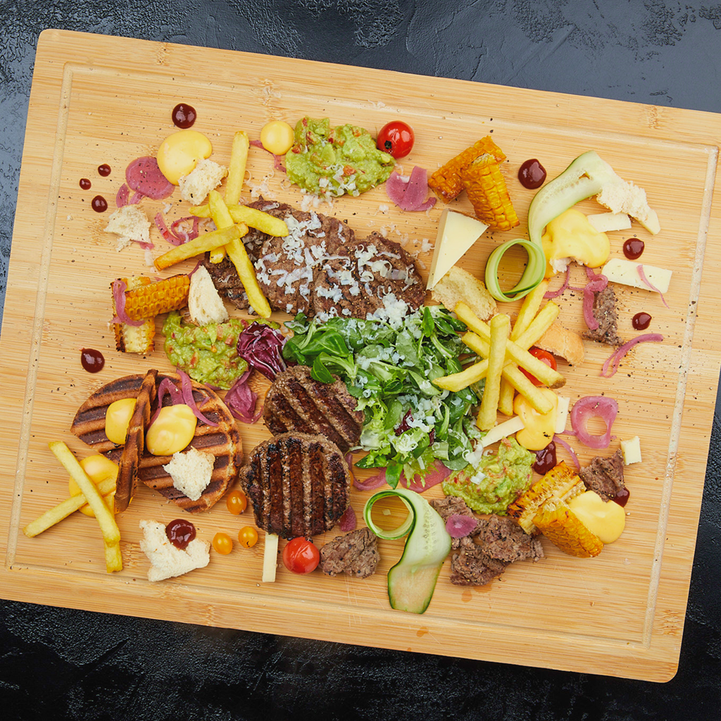 Burgerplatte mit Dry Aged Beef Patties, Pommes frites, Guacamole, Melted Cheese Dip, Feldsalat, Mais, Classic Burger Buns, Kirschtomaten, Radicchio, Gurke, Grana Padano und Mojo Rojo Dip.