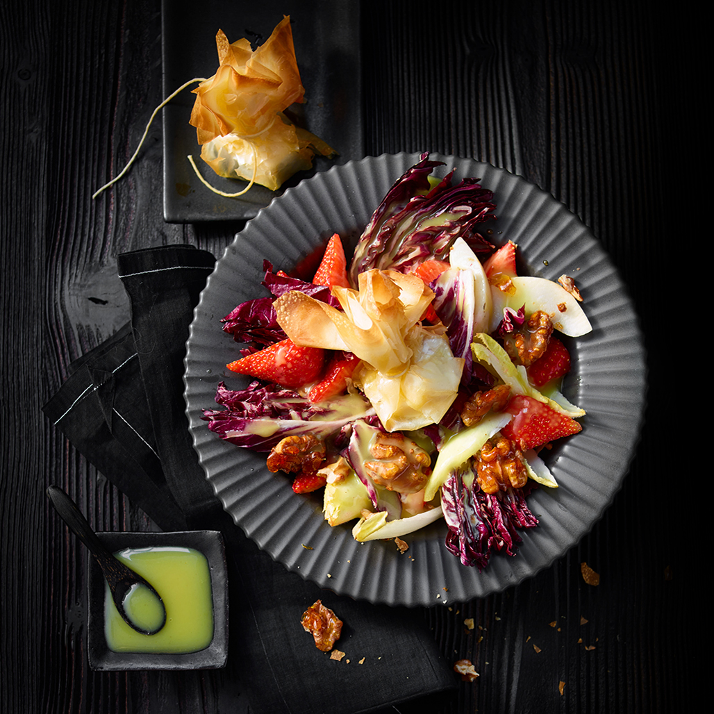 Salat mit Erdbeeren, Radicchio, Walnüssen und Honey Mustard Vinaigrette auf schwarzem Teller